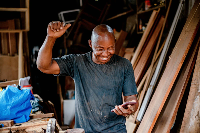 Carpenter celebrating good news on his phone in the workshop